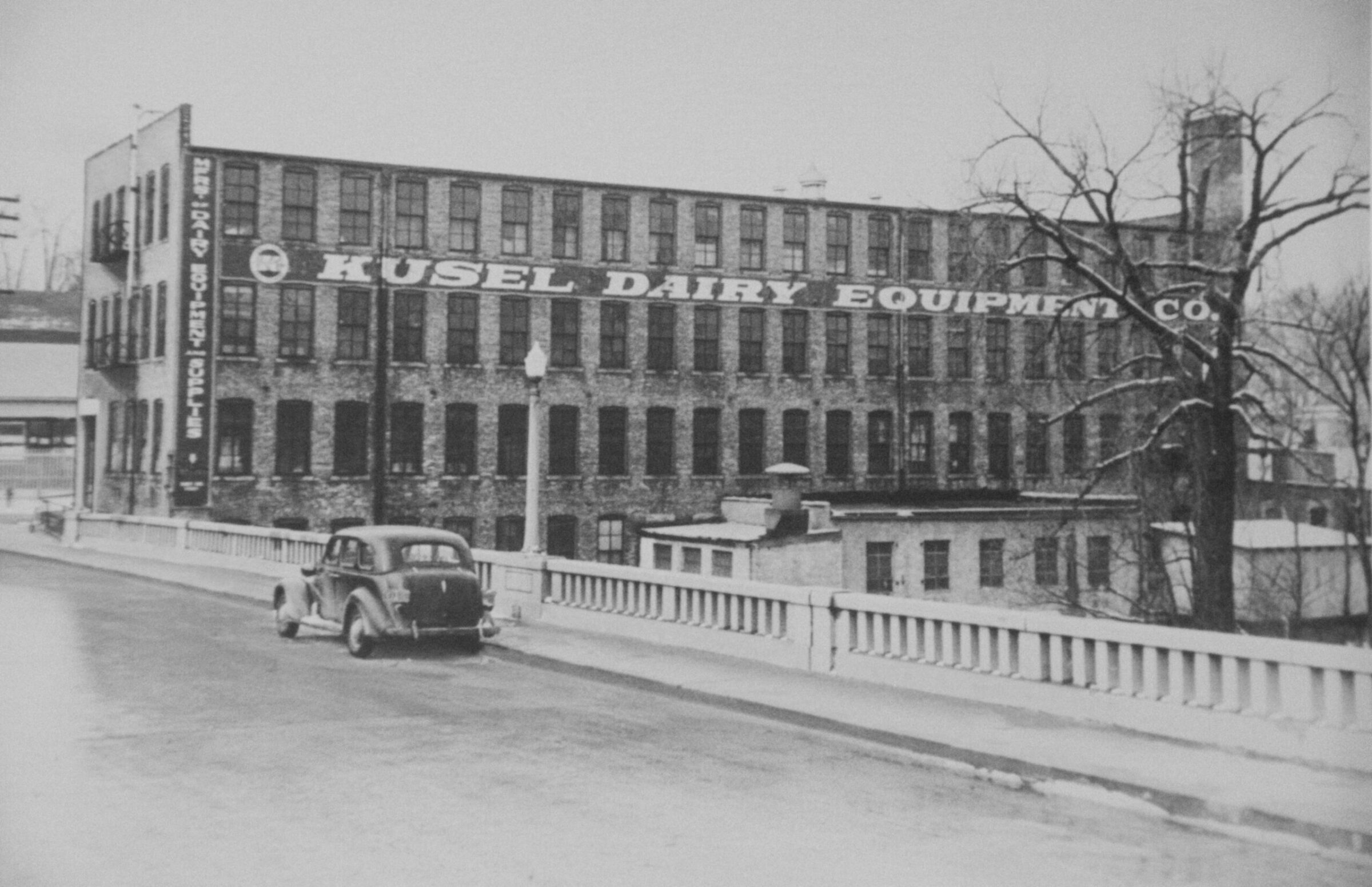Kusel Dairy Equipment Co. factory building with a vintage car on a bridge.