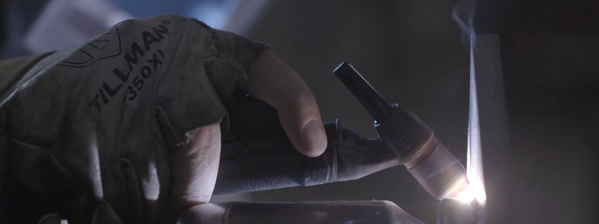 Welder's gloved hand holding a torch, creating a bright arc on metal.